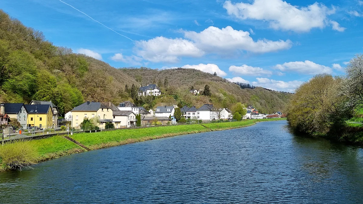 The village of Stolzembourg on the banks of the Our, with pale houses below wooded hills under a blue sky