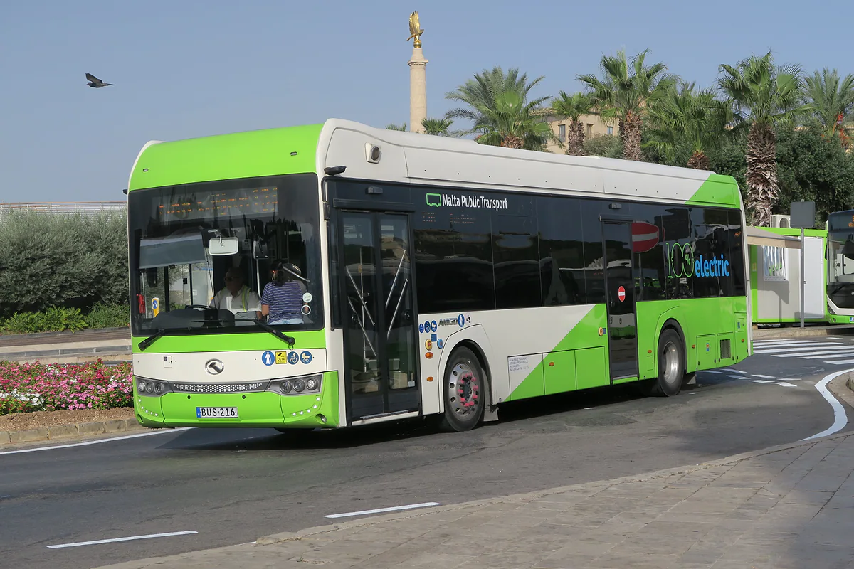 Un autobús verde y blanco de Malta Public Transport girando en una rotonda con palmeras, el transporte público que recorre toda la isla.