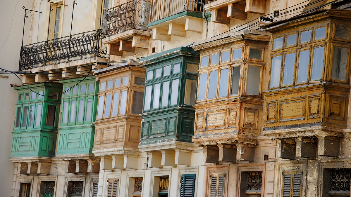 Una hilera de balcones cerrados de madera en La Valeta, pintados de verde, ocre y crema, típicos de las fachadas maltesas.