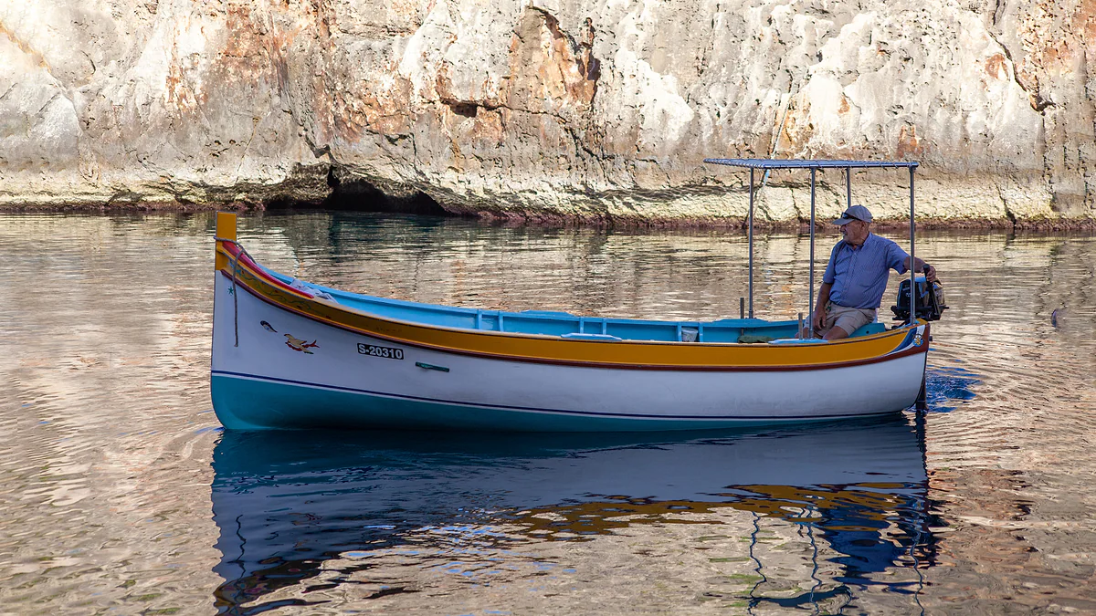 Una barca de madera pintada navegando junto a los acantilados de Wied iż-Żurrieq, de camino a recoger a los visitantes de la Blue Grotto.