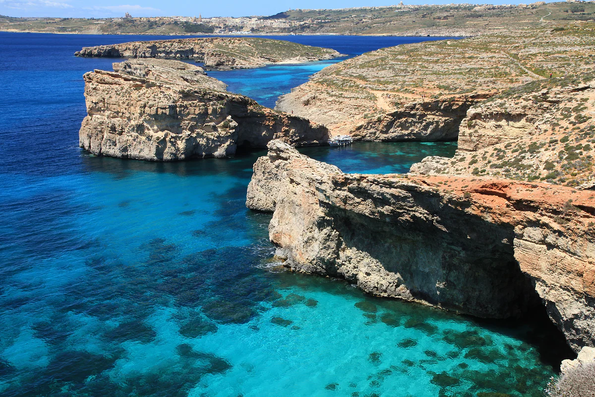 El agua turquesa de la Blue Lagoon de Comino entre los islotes de roca y Cominotto, con Gozo y Malta al fondo en un día despejado.