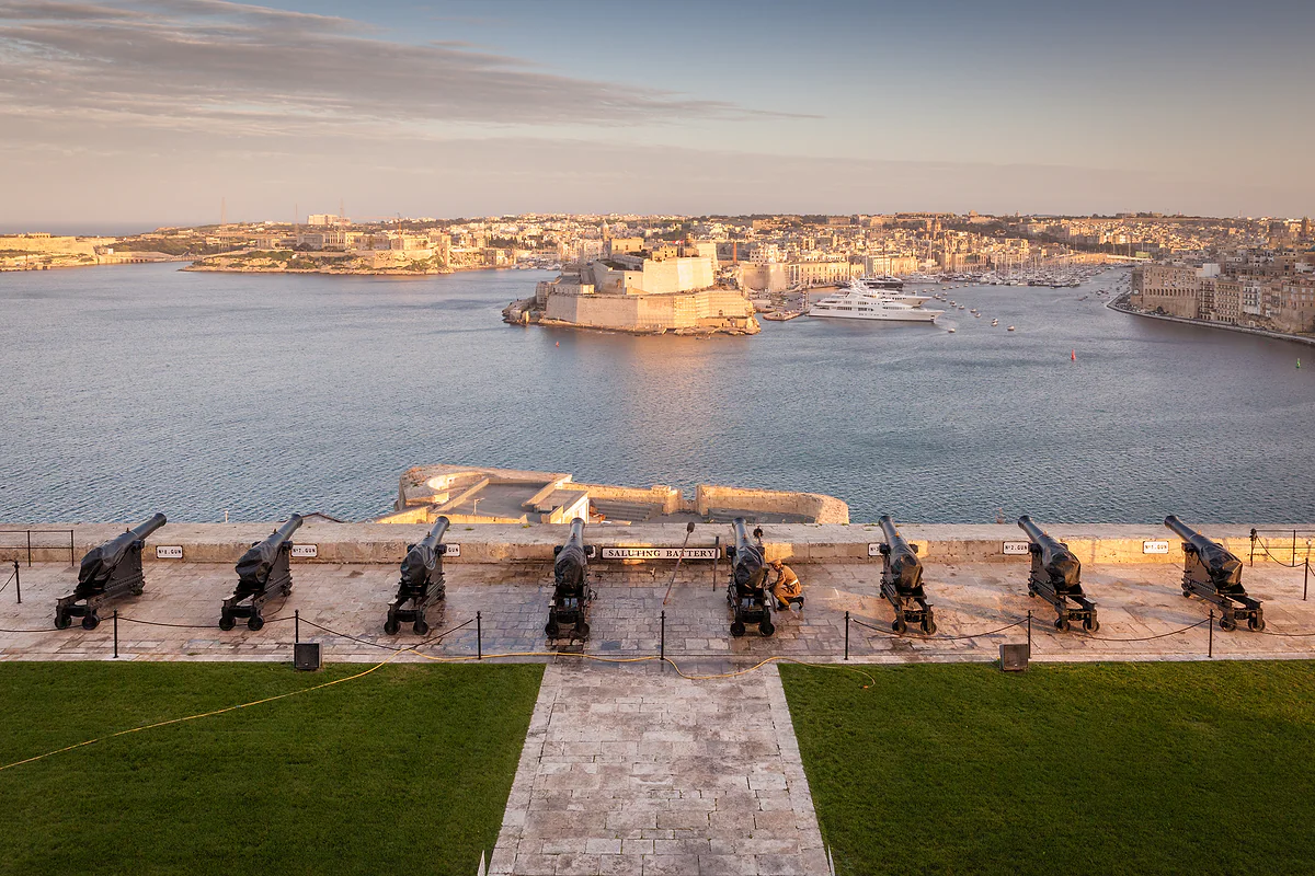 La fila de cañones de la Saluting Battery de La Valeta al atardecer, con el fuerte San Ángel y Birgu al otro lado del Gran Puerto.