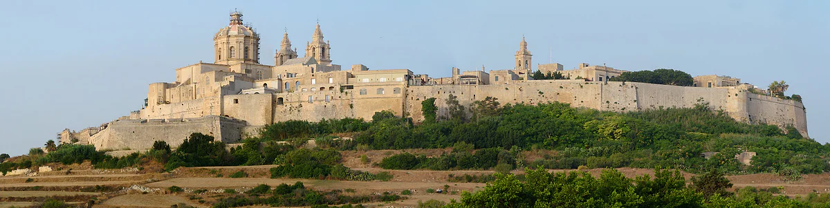 Mdina amurallada sobre su colina, con la cúpula de la catedral de San Pablo sobresaliendo de las murallas y los campos de Malta delante.