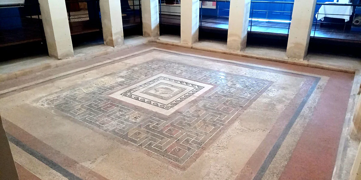 El mosaico geométrico del peristilo de la casa romana de Rabat, con su cenefa en relieve óptico, conservado bajo techo.