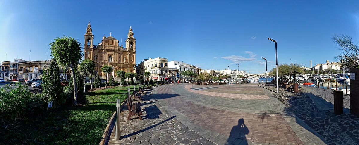 La plaza junto al puerto deportivo de Msida con la iglesia parroquial de San José al fondo, bajo un cielo despejado.