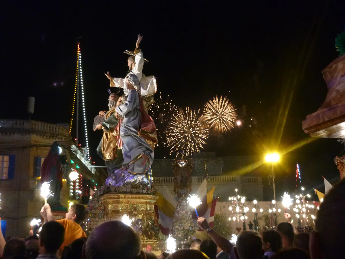 La estatua del Salvador llevada en procesión por las calles de Lija al cierre de su festa, con la gente, las luces y los fuegos detrás.