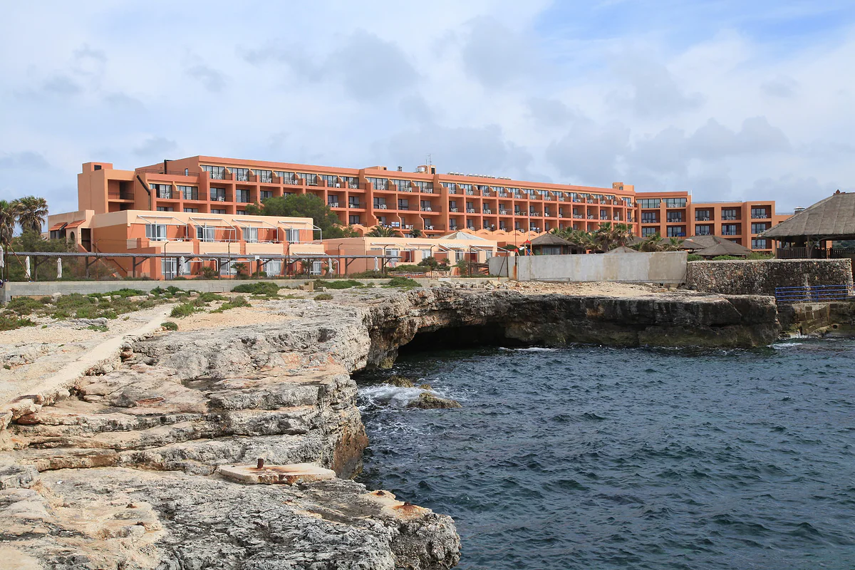 Ramla Bay Resort on the Marfa peninsula, its terracotta blocks rising above the limestone shore with open sea in front.