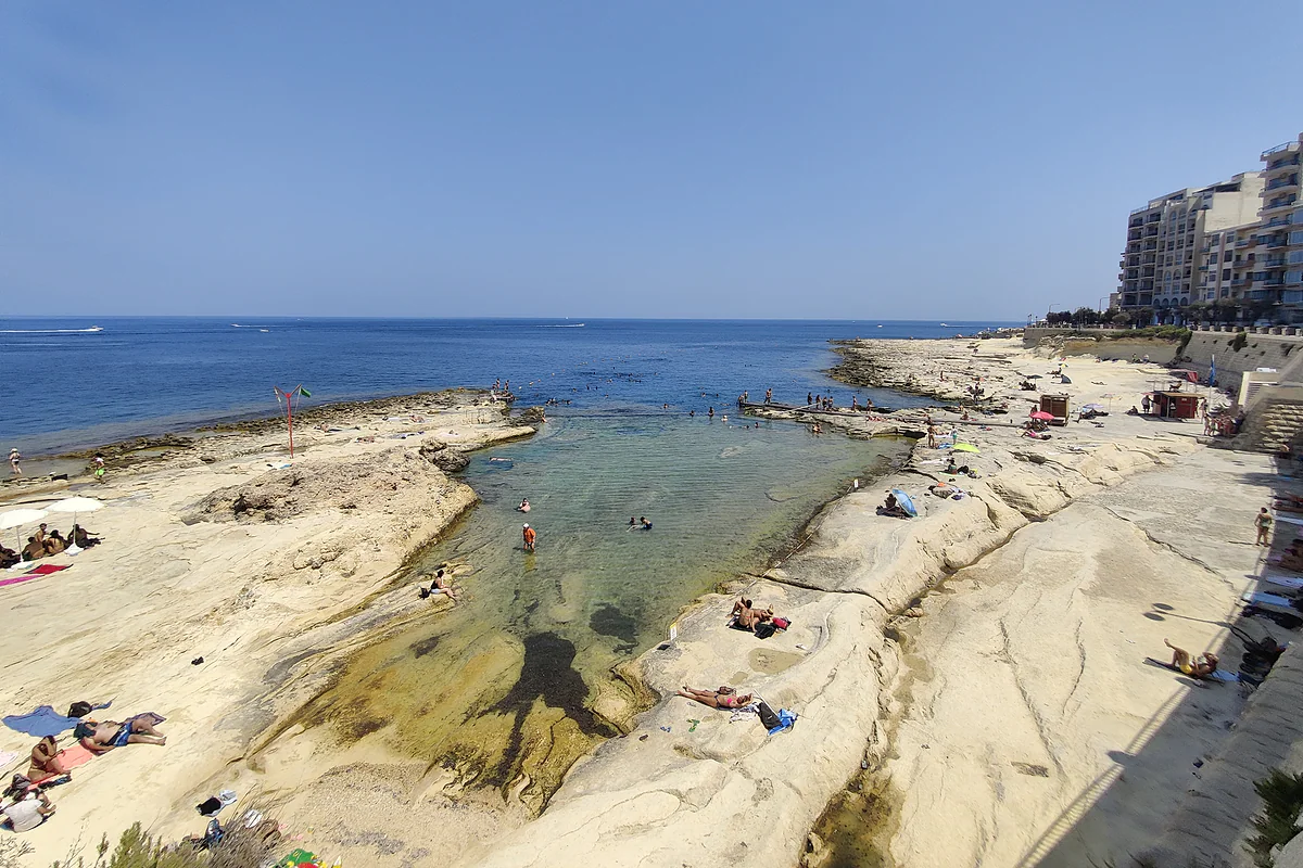 Las rocas planas de Fond Għadir en Sliema, donde la gente se baña en pozas de agua clara junto a los edificios del paseo marítimo.
