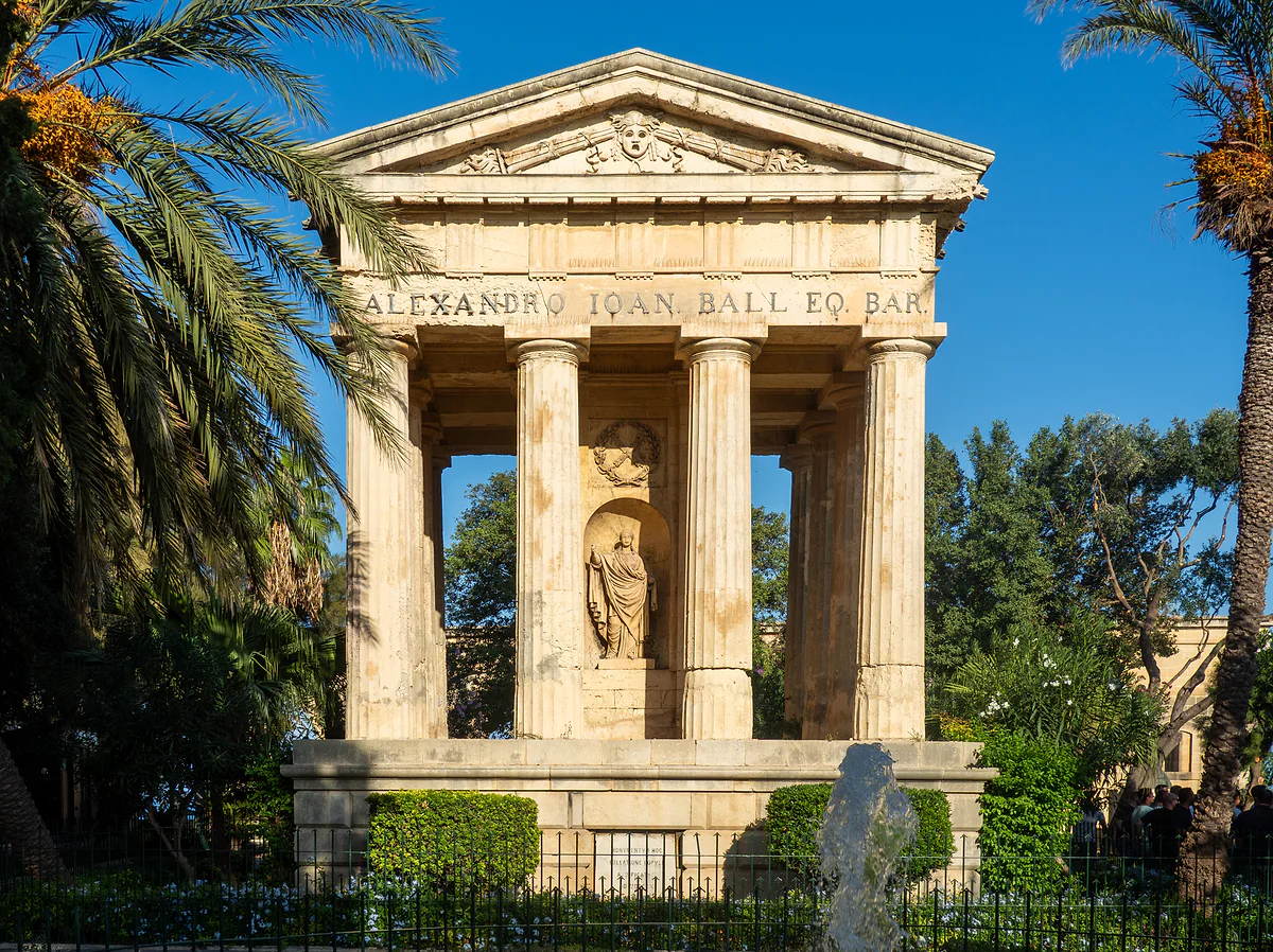 El templete neoclásico dedicado a Alexander Ball en los jardines Lower Barrakka de La Valeta, entre palmeras y bajo un cielo azul intenso.