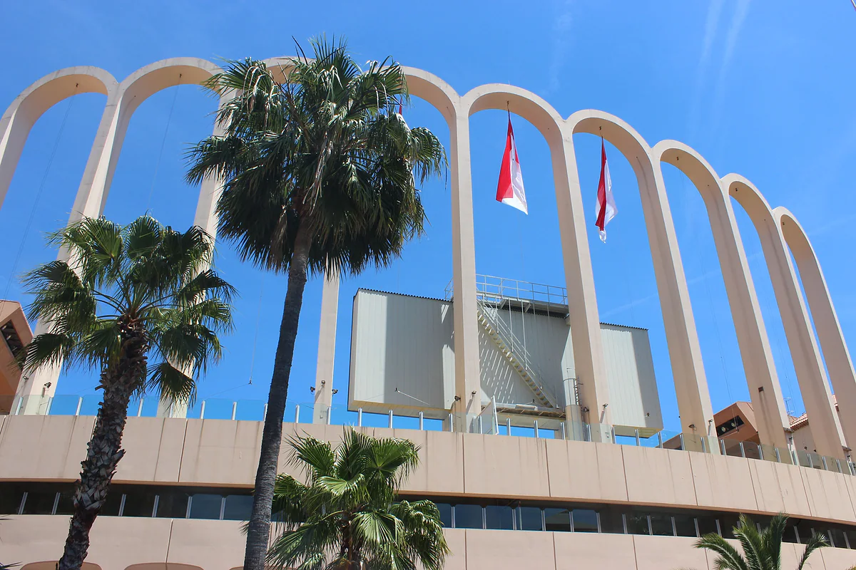 Los arcos blancos del estadio Louis II con banderas de Mónaco y palmeras delante.