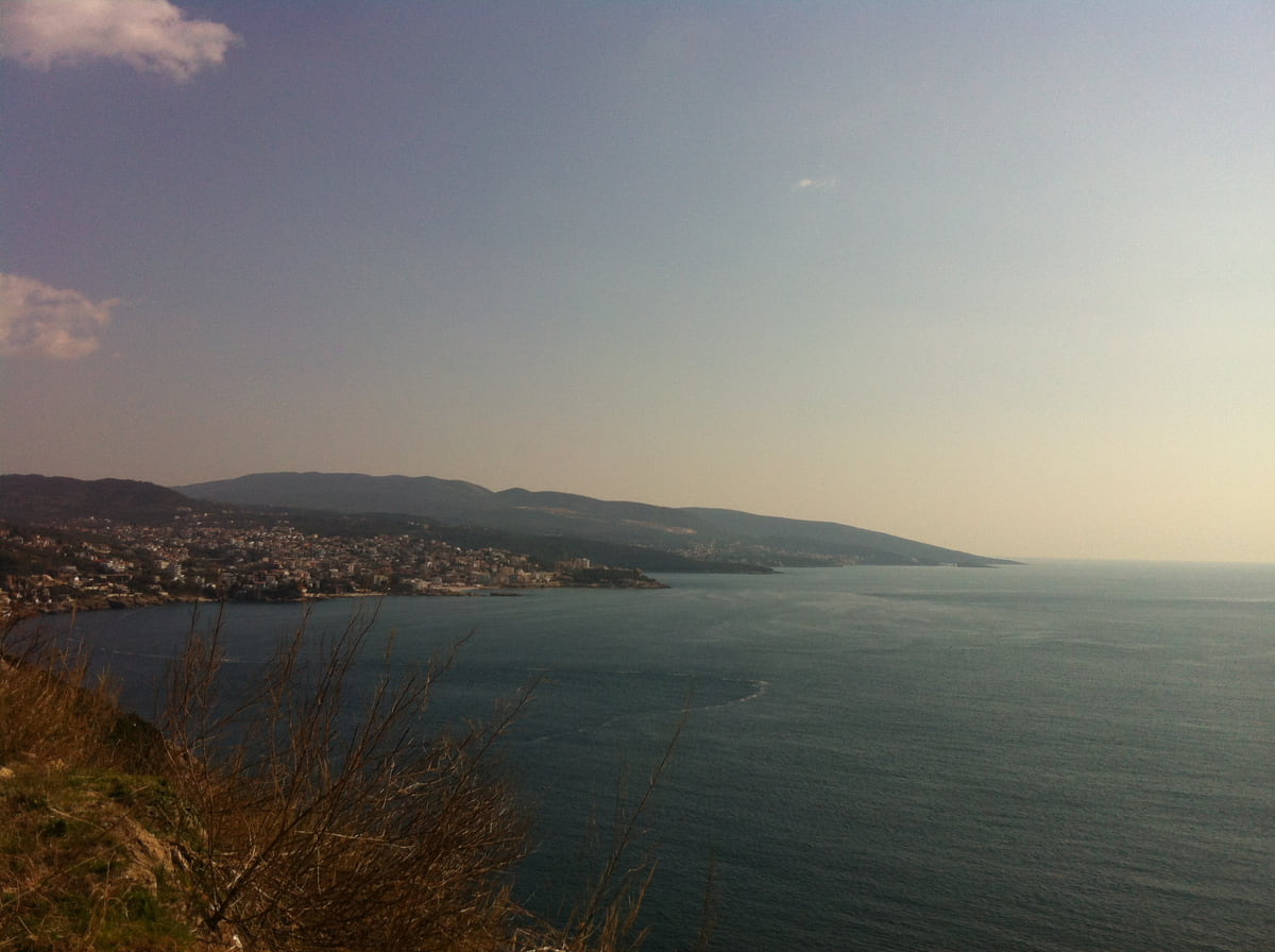 Dobra Voda bay from the hillside, with houses along the shore, hilly coastline beyond and dry scrub in the foreground