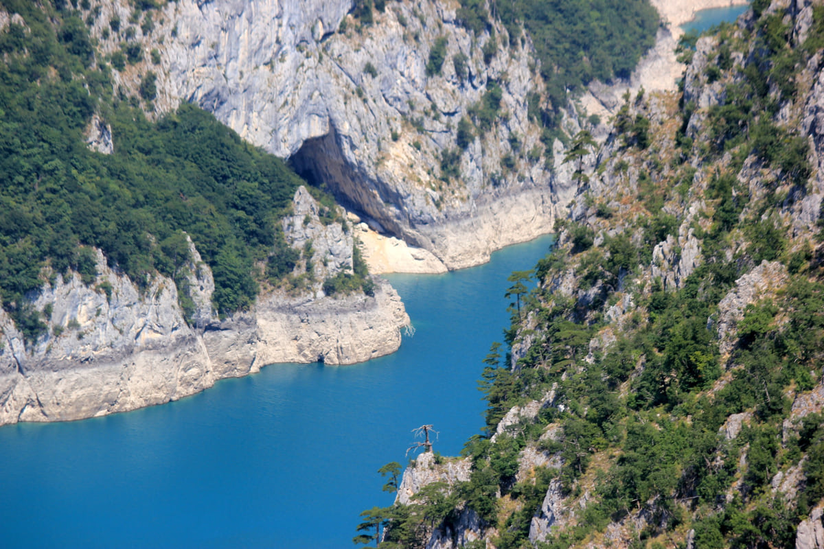 The Piva canyon with the blue water of the reservoir between pale rock walls and forest on the slopes