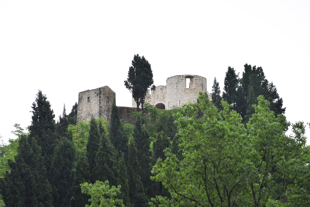 The stone towers of Besac fortress rising above cypresses and pines on top of the hill that overlooks Virpazar