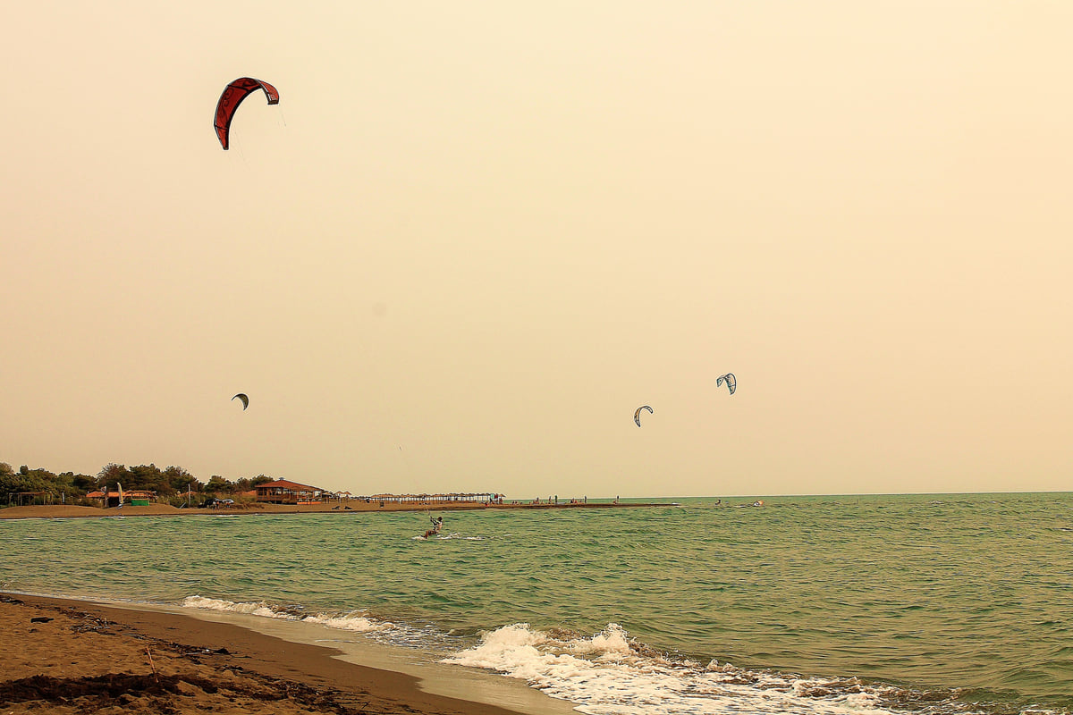 Kitesurf kites over the sea at Velika Plaža in Ulcinj, with gentle waves breaking on the sandy shore
