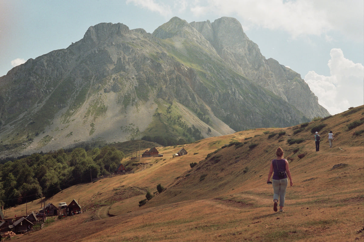A trail across the Štavna meadows towards the Komovi peaks, with small hikers in front of the great rock massif