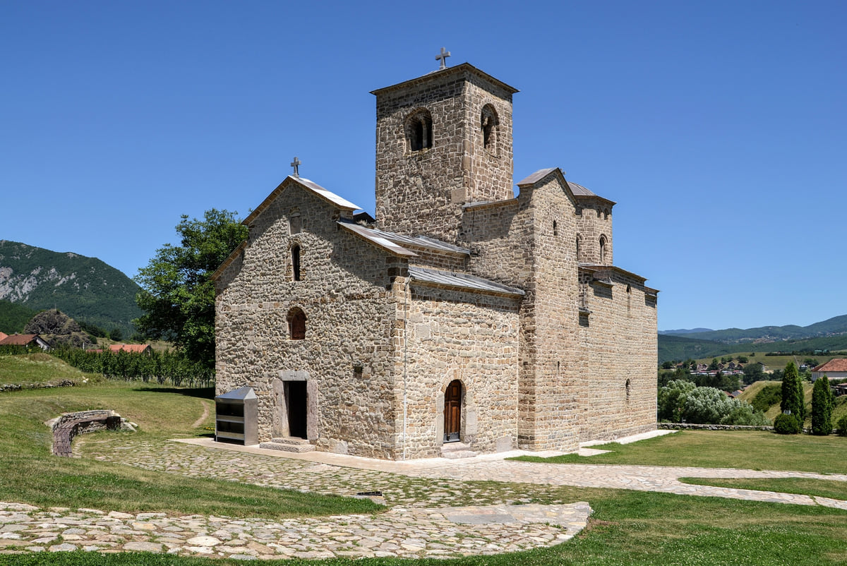 The stone church of Đurđevi Stupovi monastery in Berane, with its tower over the entrance and a cobbled courtyard under a blue sky
