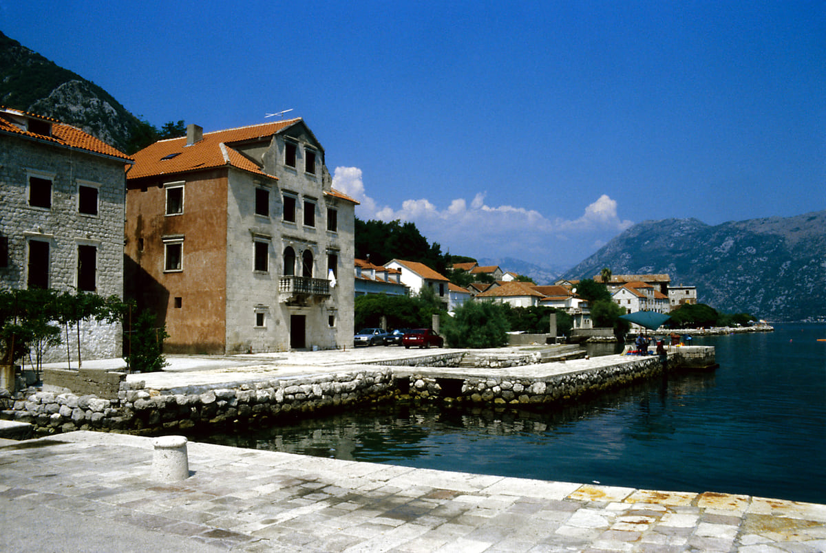 The quay at Prčanj with stone captains' houses beside the water of the Bay of Kotor and mountains beyond