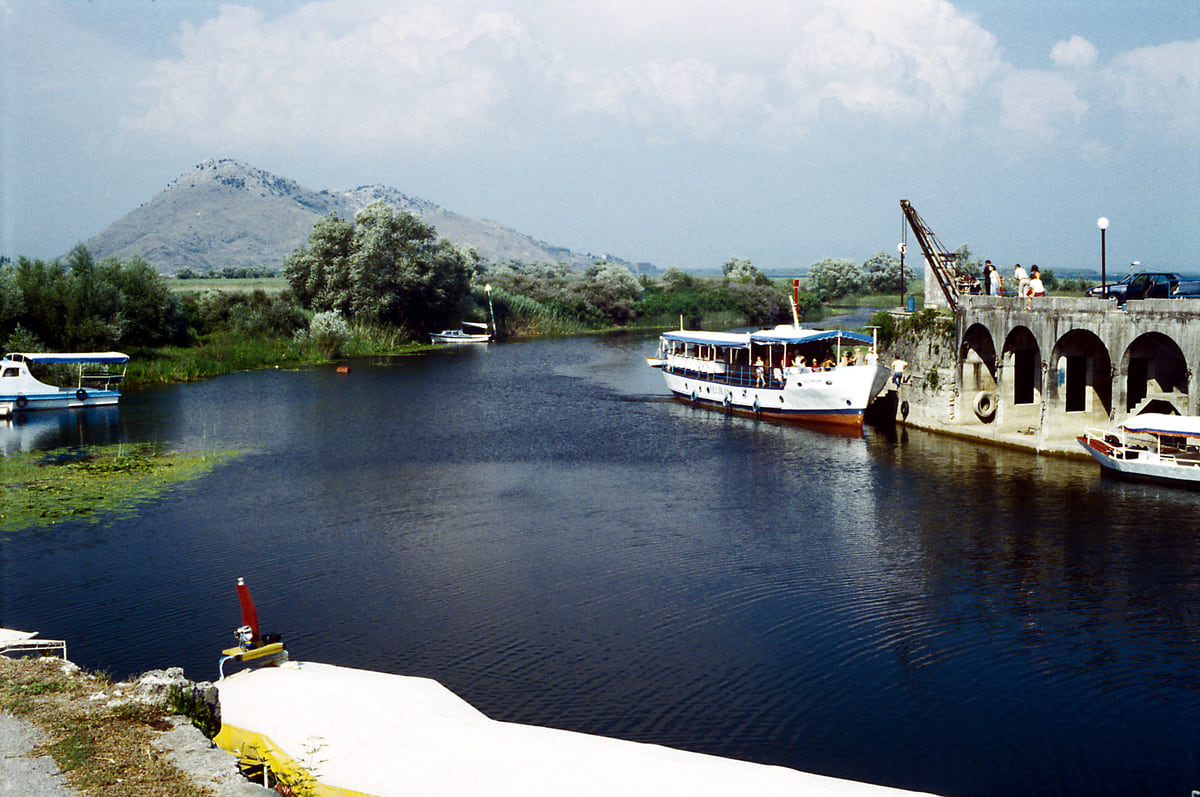 The small harbour at Virpazar on Lake Skadar, with excursion boats moored along the channel and mountains behind