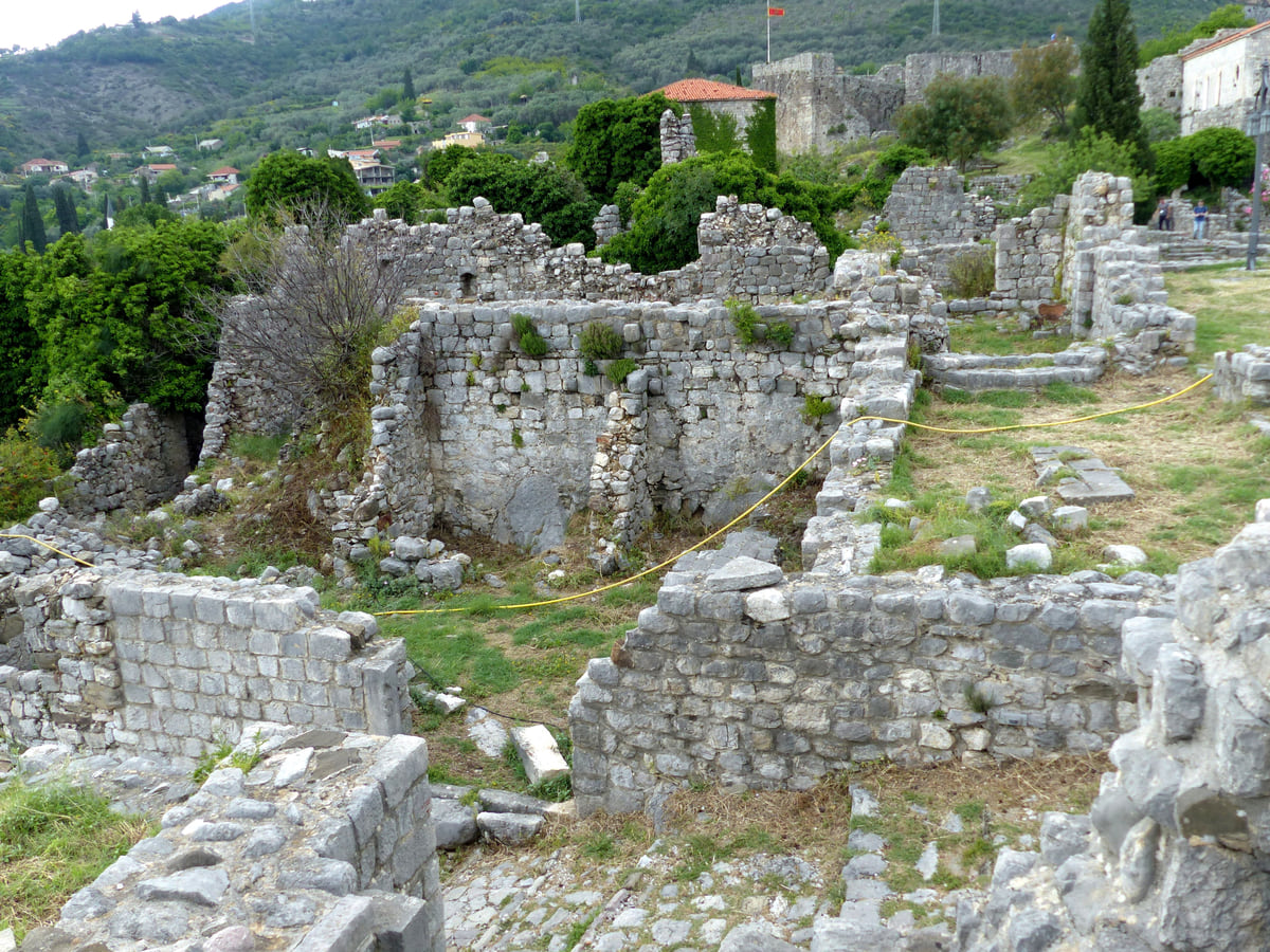 Ruined stone houses in Stari Bar among grass and trees, with roofless walls and the green hillside behind