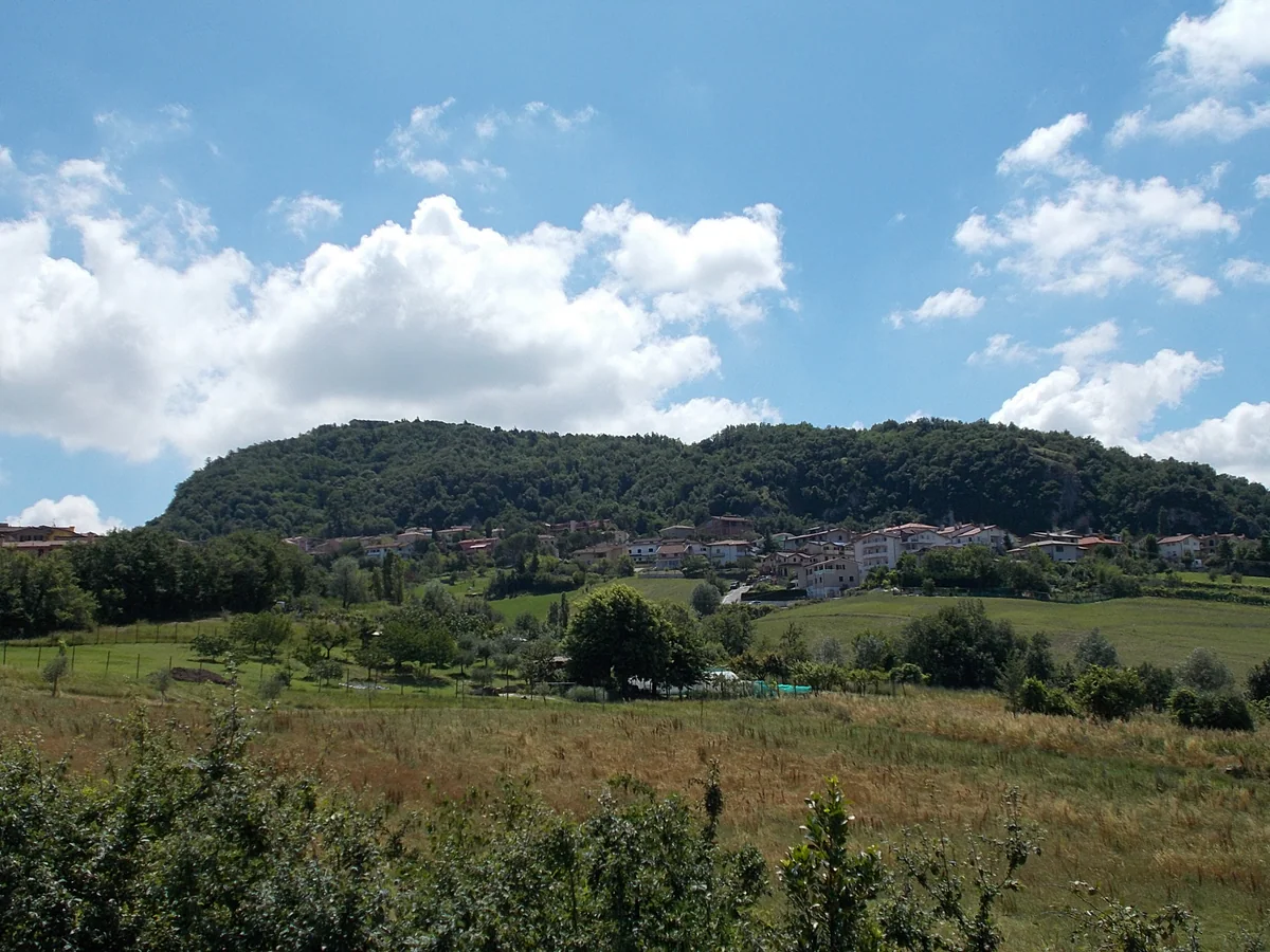 Prados de Acquaviva con las casas al pie de Montecerreto, la colina boscosa donde está el parque de La Pineta, bajo un cielo con nubes.