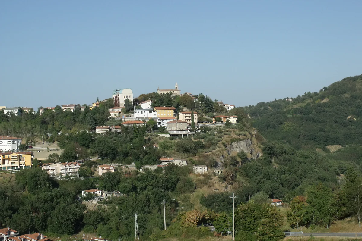 Faetano visto desde lo alto, con casas de tejados rojos entre prados y bosquecillos que bajan hacia el valle del Marano.