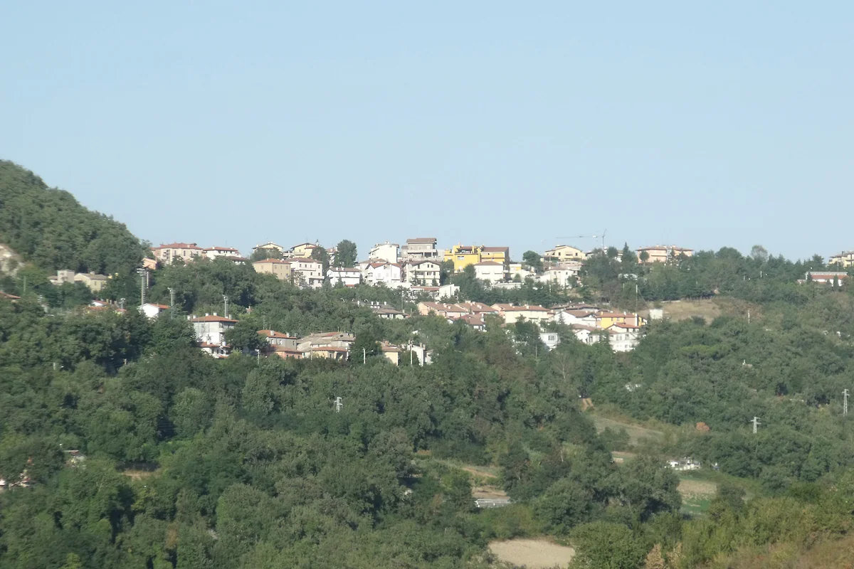 Las casas de Fiorentino en lo alto de una loma cubierta de bosque, vistas desde el valle en un día despejado.