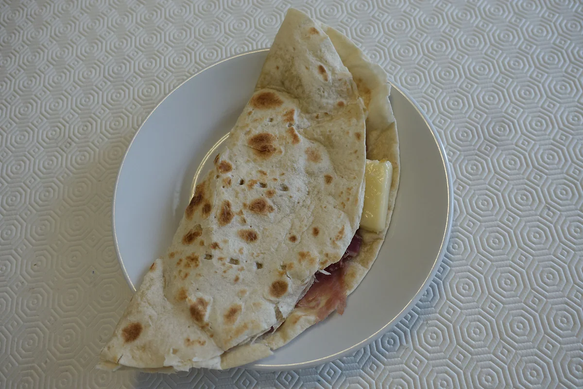 Una piadina doblada y rellena de jamón y queso en un plato blanco: el pan plano de la Romaña que se come en todo San Marino.