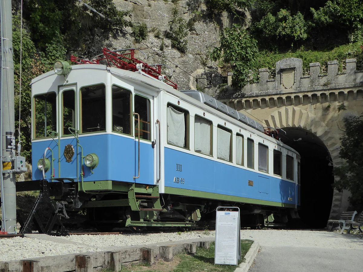La automotriz blanca y azul del antiguo tren de Rímini a San Marino, expuesta en la vía ante la boca almenada de la galería Montale.