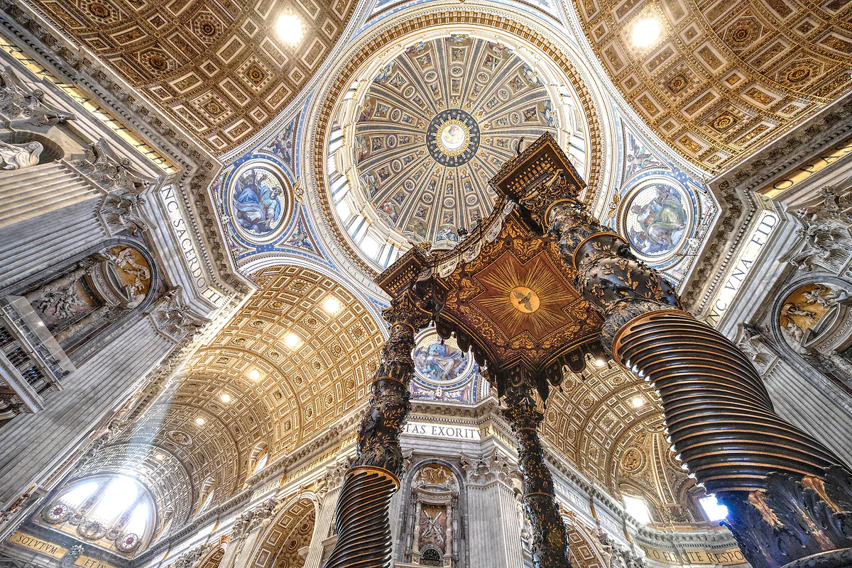 Baldaquino de bronce de Bernini visto desde abajo, con la cúpula de San Pedro y los rayos de luz que entran por sus ventanas.