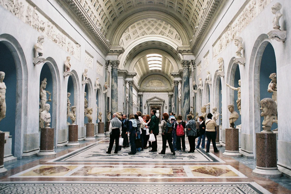 El Braccio Nuovo de los Museos Vaticanos, galería neoclásica con estatuas en nichos, bustos sobre ménsulas, bóveda de casetones y suelo de mosaico.