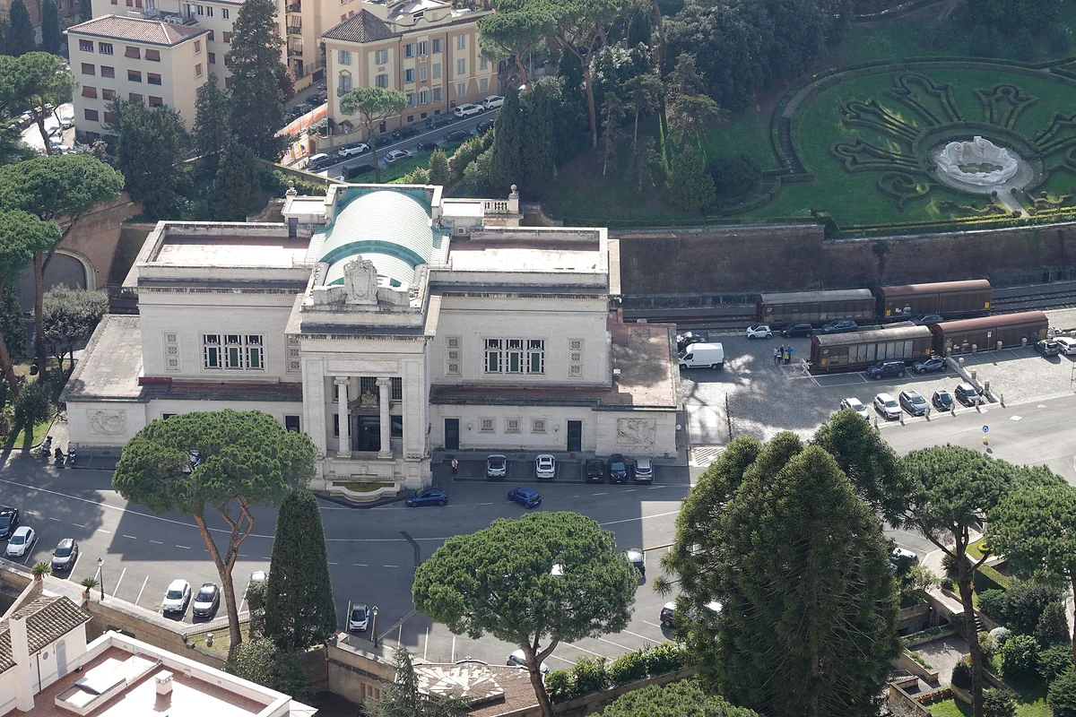 La estación de tren del Vaticano, de mármol blanco y cúpula de cobre verde, vista desde la cúpula de San Pedro, con vagones y los Jardines detrás.