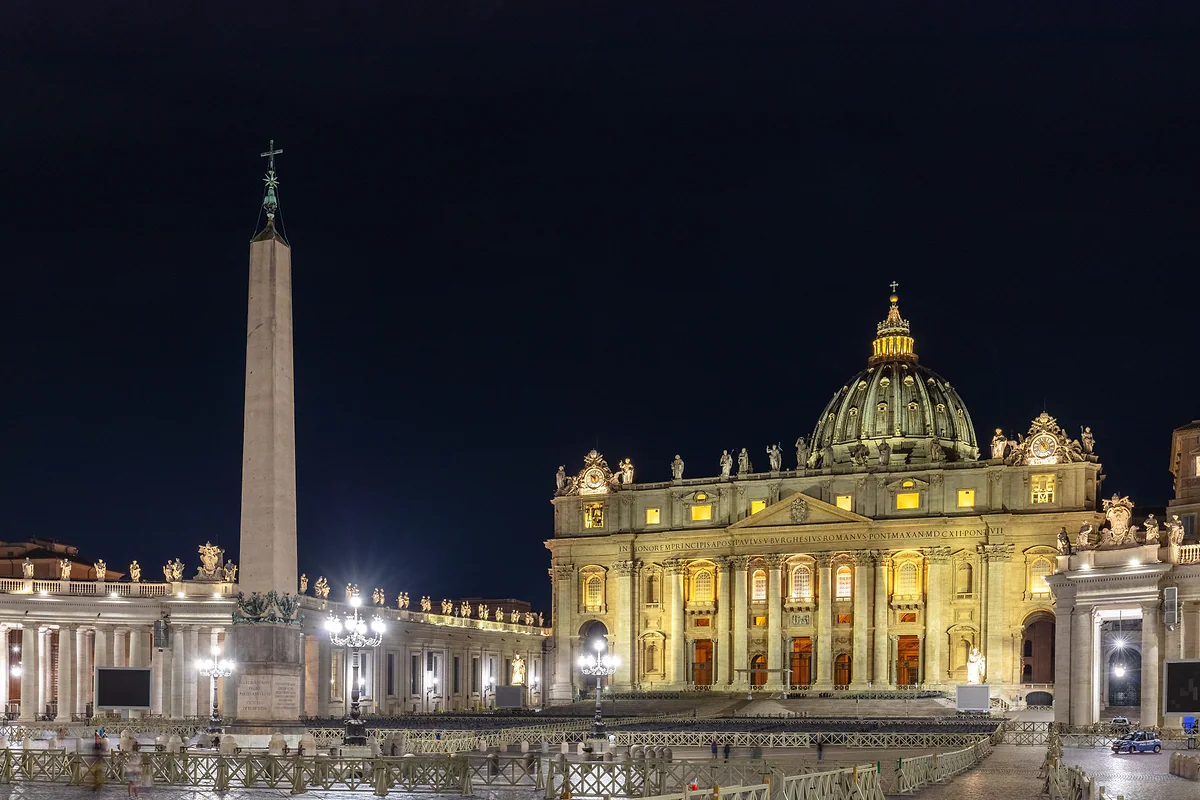 El obelisco de la plaza de San Pedro y la basílica iluminada de noche, con la columnata de Bernini a la izquierda.
