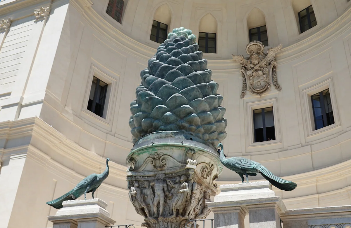 La Piña de bronce del Patio de la Piña, sobre su capitel antiguo y entre dos pavos reales de bronce, delante del gran nicho de Pirro Ligorio.